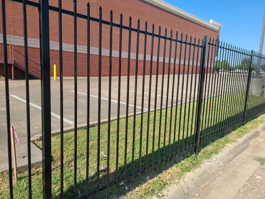 Black steel picket fence along a commercial parking lot